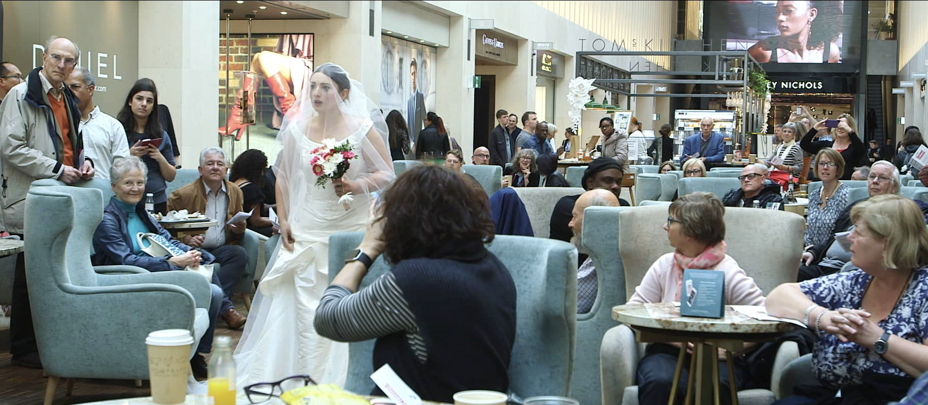 A woman in a wedding dress passes through a café.